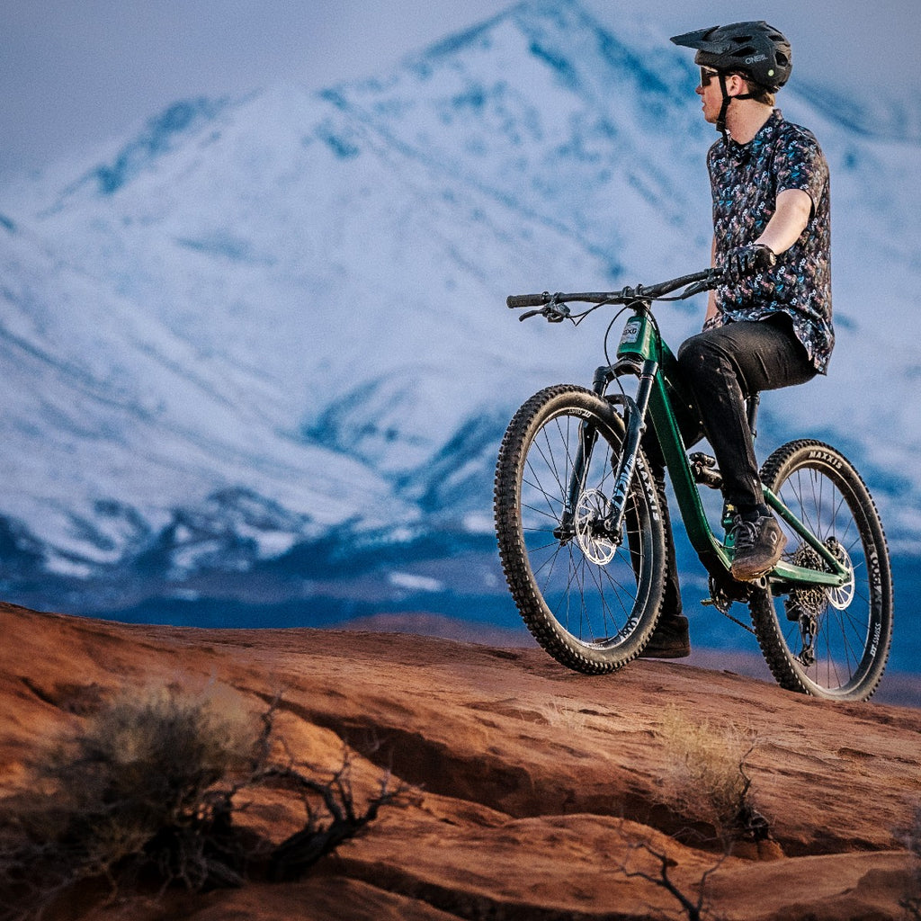 Mountain biker sitting on Guerrilla Gravity full suspension bike with snow capped peaks in the background mobile view