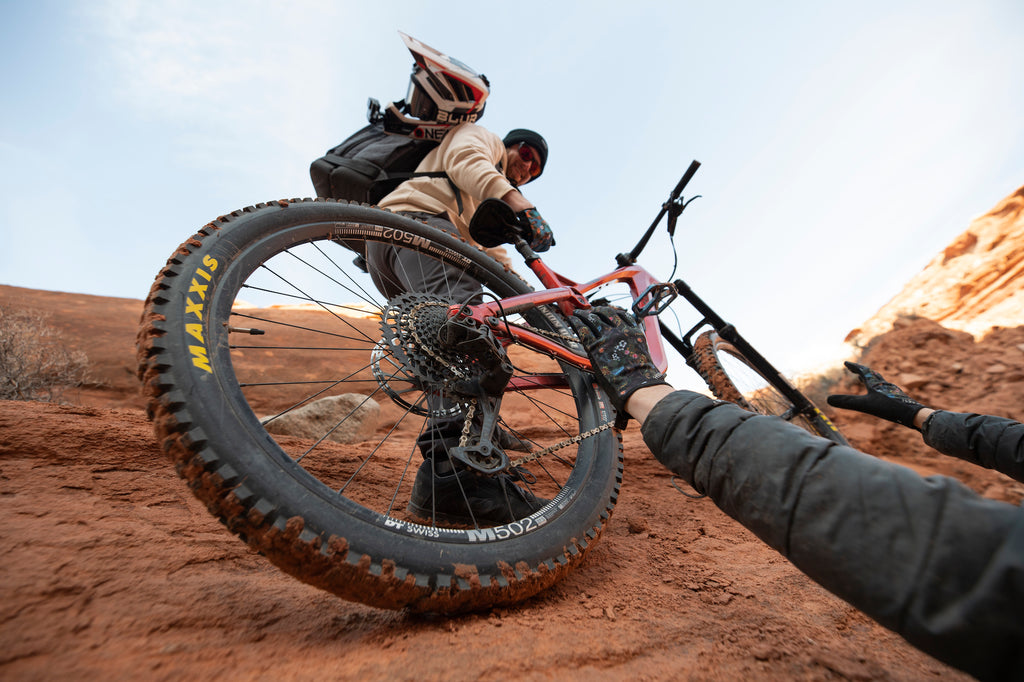 Two people lifting Guerrilla Gravity bike up a red rock feature